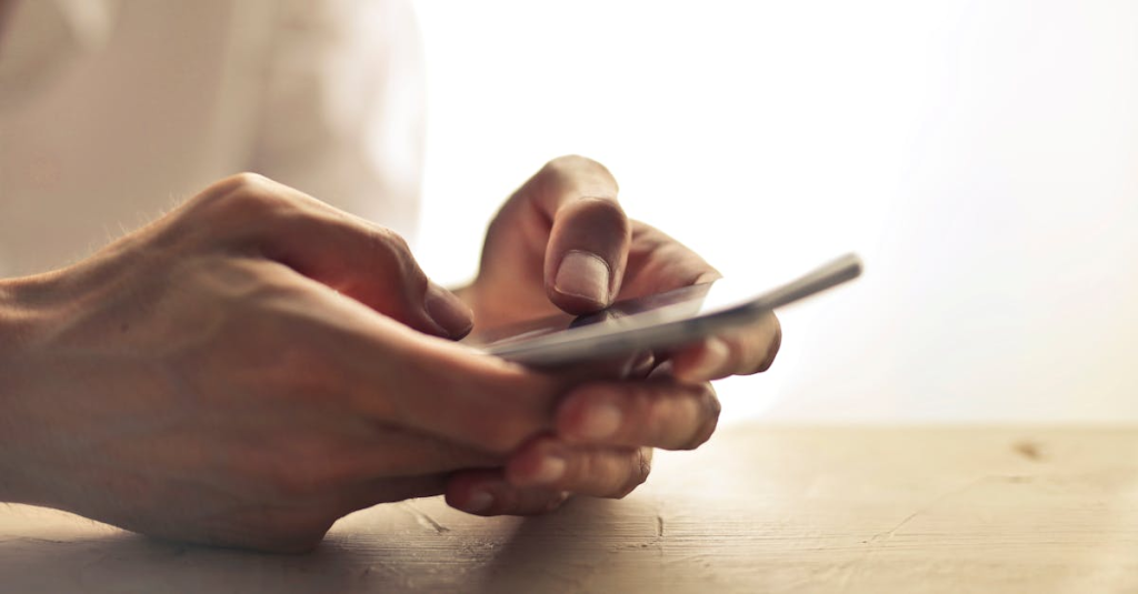Close-up of an individual's hands holding a smartphone on a table indoors.
